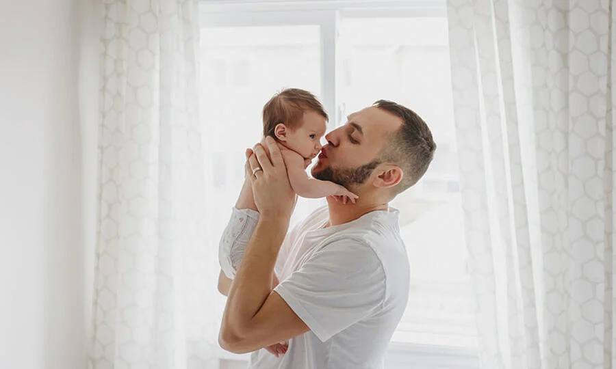 First-time home buyer planting a kiss on the nose of a baby in a very, very, very white room